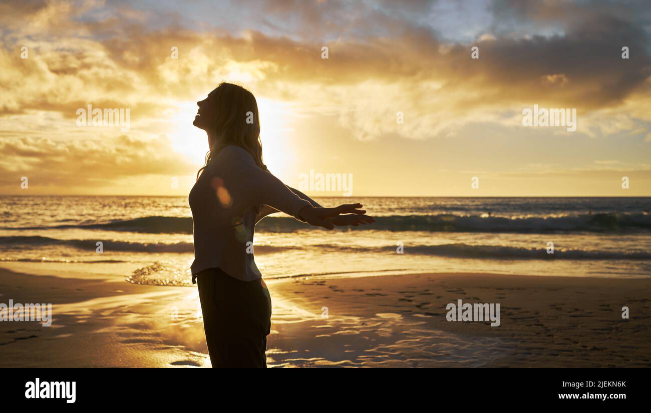 Silueta de una mujer en la playa al atardecer afuera. Perfil de la mujer estirando sus brazos detrás de ella en la sensación de la orilla del mar libre. Mujer relajada Foto de stock
