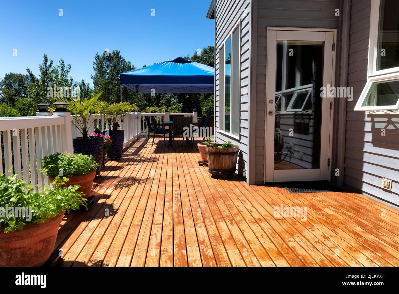 Casa con terraza de madera con muebles de exterior y jardín trasero durante el verano Foto de stock