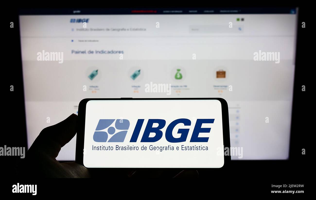 Persona que sostiene el celular con el logo del Instituto Brasileiro de Geografia e Estatitica (IBGE) en la pantalla con la página web. Enfoque la pantalla del teléfono. Foto de stock