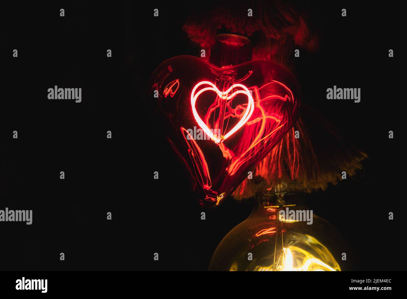 Bombilla de cristal rojo con forma de corazón que brilla en la oscuridad Foto de stock
