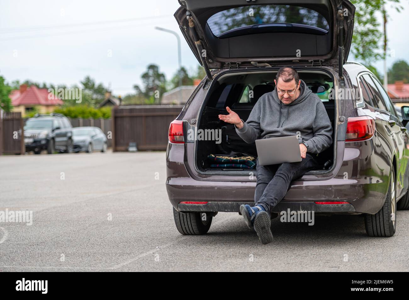 un hombre sentado en el maletero abierto de un coche y trabajando en un  portátil, tecnología para trabajar a distancia Fotografía de stock - Alamy