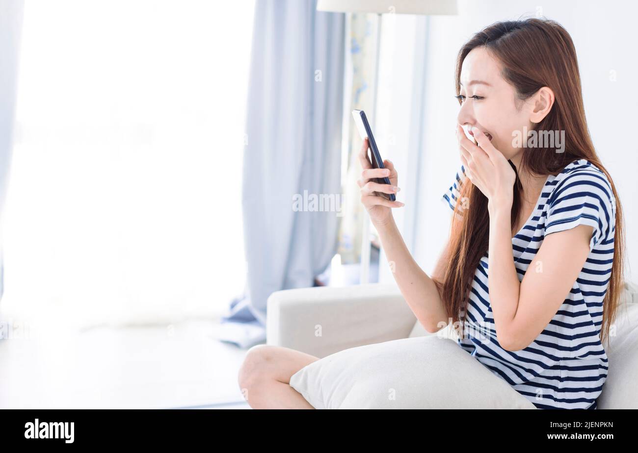 Una joven sorprendida mirando la pantalla del smartphone en el sofá de la casa Foto de stock