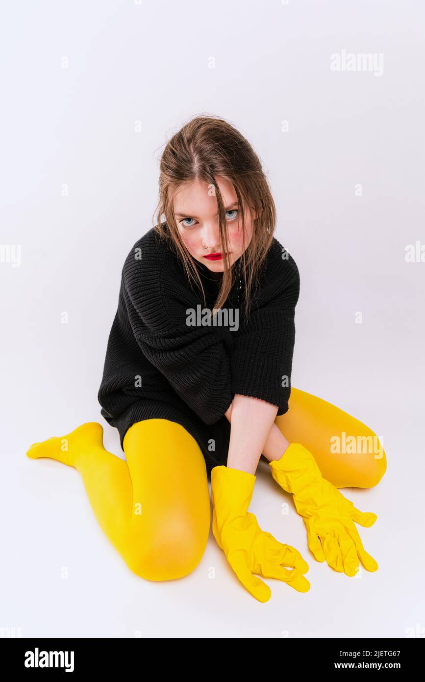 Retrato de niña en chaqueta negra, medias amarillas y guantes de goma,  sentada en el suelo, mirando a la cámara, posando aislada sobre un estudio  gris Fotografía de stock - Alamy