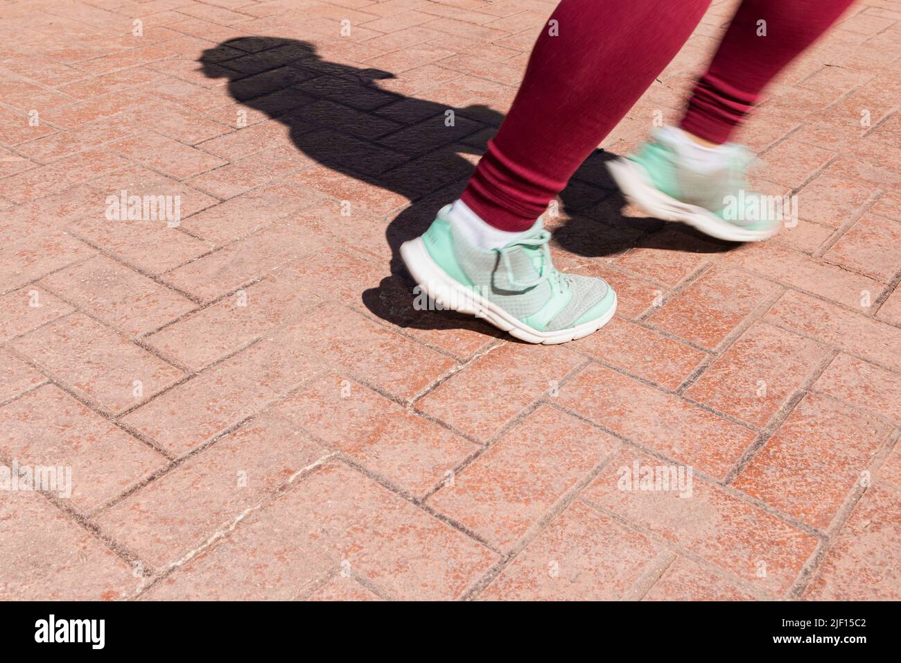 En un pavimento de concreto estampado se pueden ver los pies de una persona irreconocible que corre. Las extremidades son borrosas por el movimiento. Foto de stock