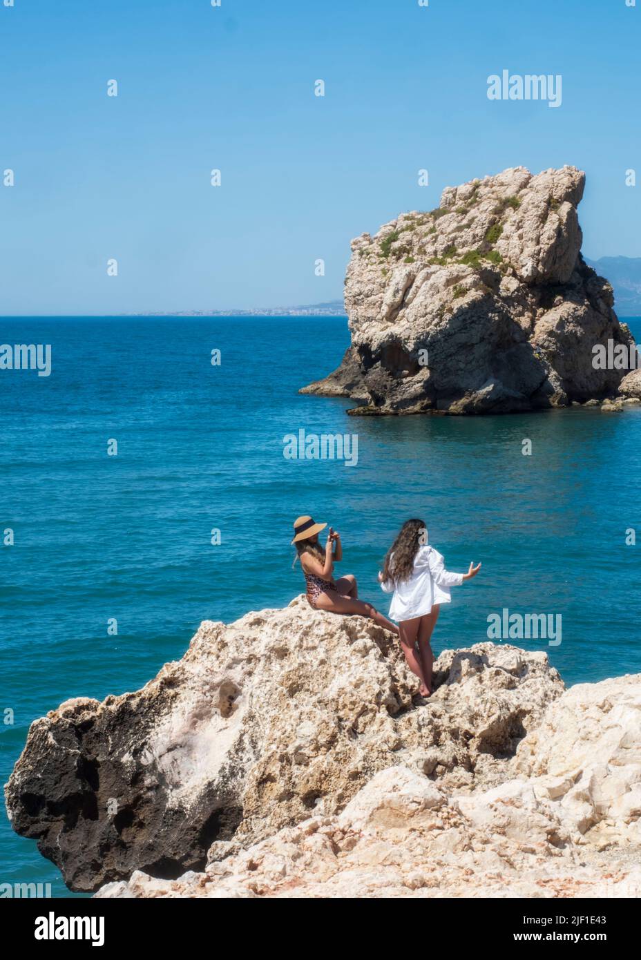 Dos jóvenes sentadas en un acantilado en la costa de Málaga frente al mar. Foto de stock