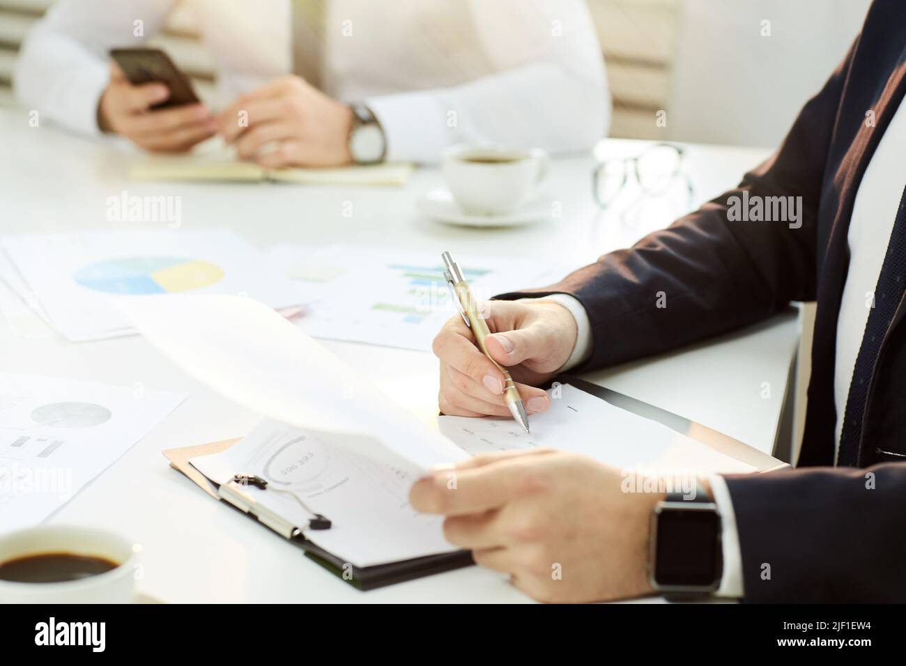 Primer plano del irreconocible hombre de negocios con traje formal sentado en una mesa de conferencias y analizando cifras financieras en una reunión Foto de stock