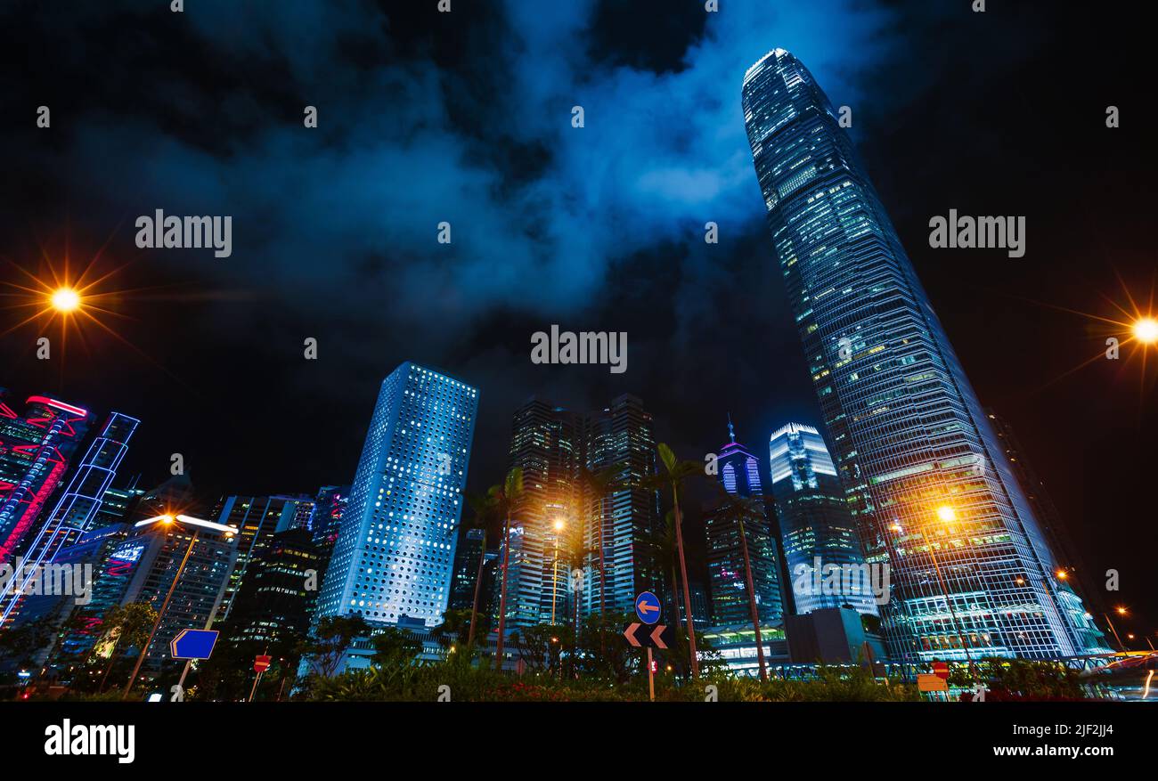 Vista nocturna de la ciudad con rascacielos bajo un cielo nublado oscuro, edificios altos de oficinas del Distrito Central de Hong Kong Foto de stock