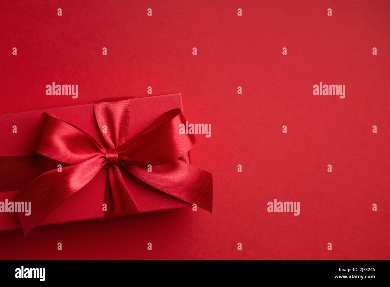 Caja de regalo roja con lazo rojo sobre fondo rojo para Navidad o San Valentín. Foto de stock