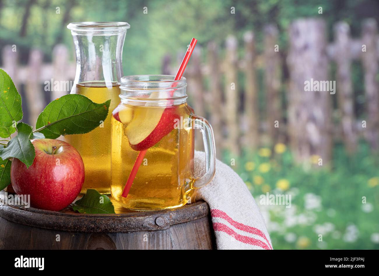 Vaso de zumo de manzana con rodaja de manzana sobre un viejo barril de madera con fondo rural Foto de stock