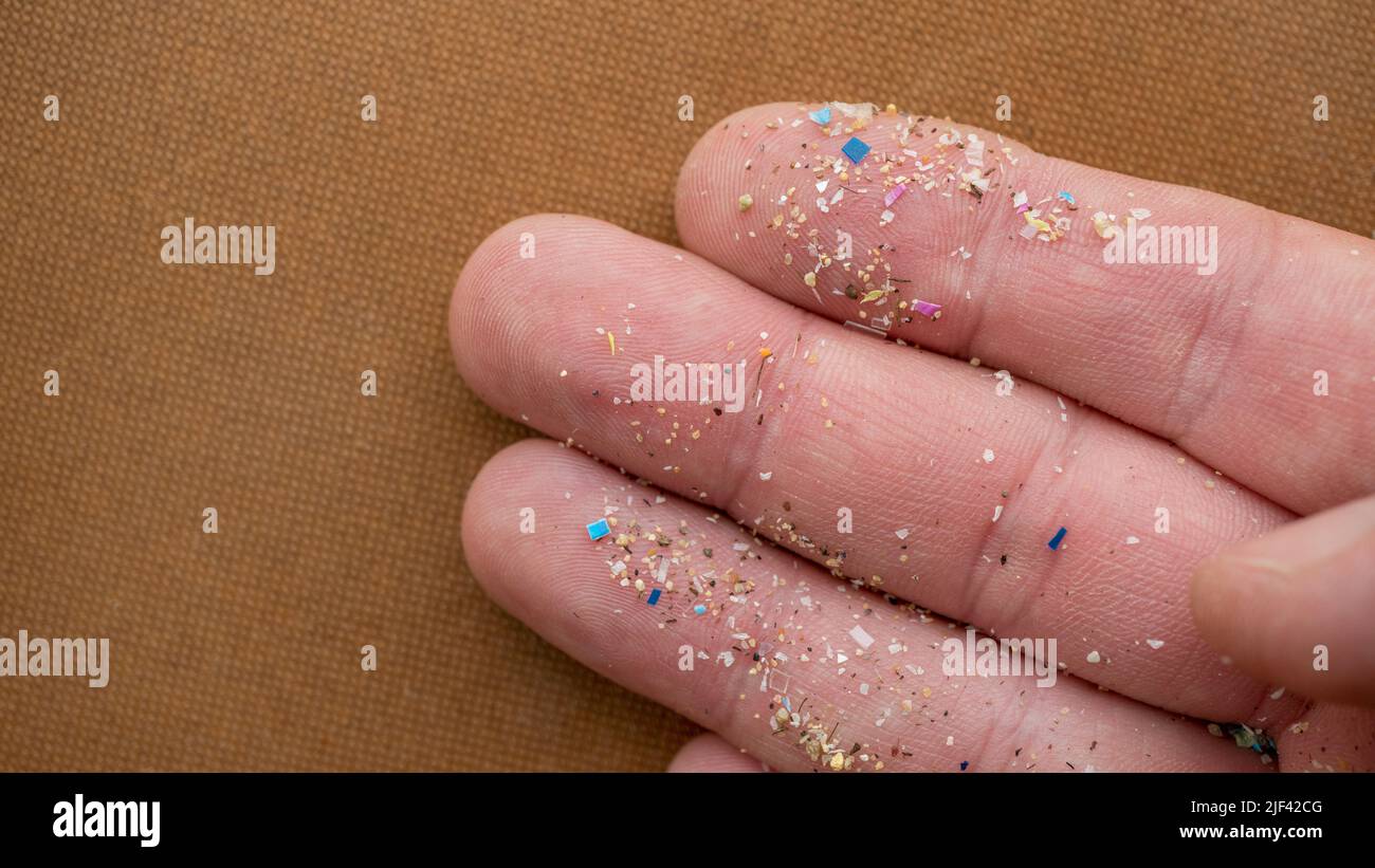 Micropartículas de plástico en un dedo humano para escamas. Concepto de contaminación del agua y calentamiento global. Foto de stock