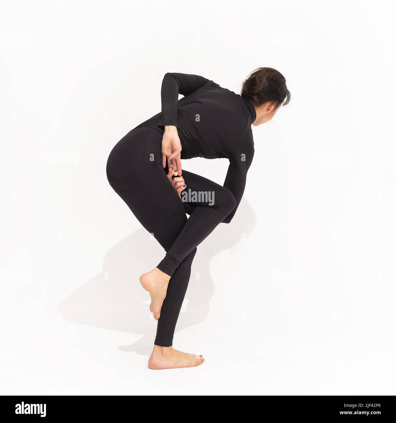 Mujer en negro sportswear practicando yoga, realiza una variación del ejercicio vatajanasana, pose de caballo sobre un fondo blanco Foto de stock