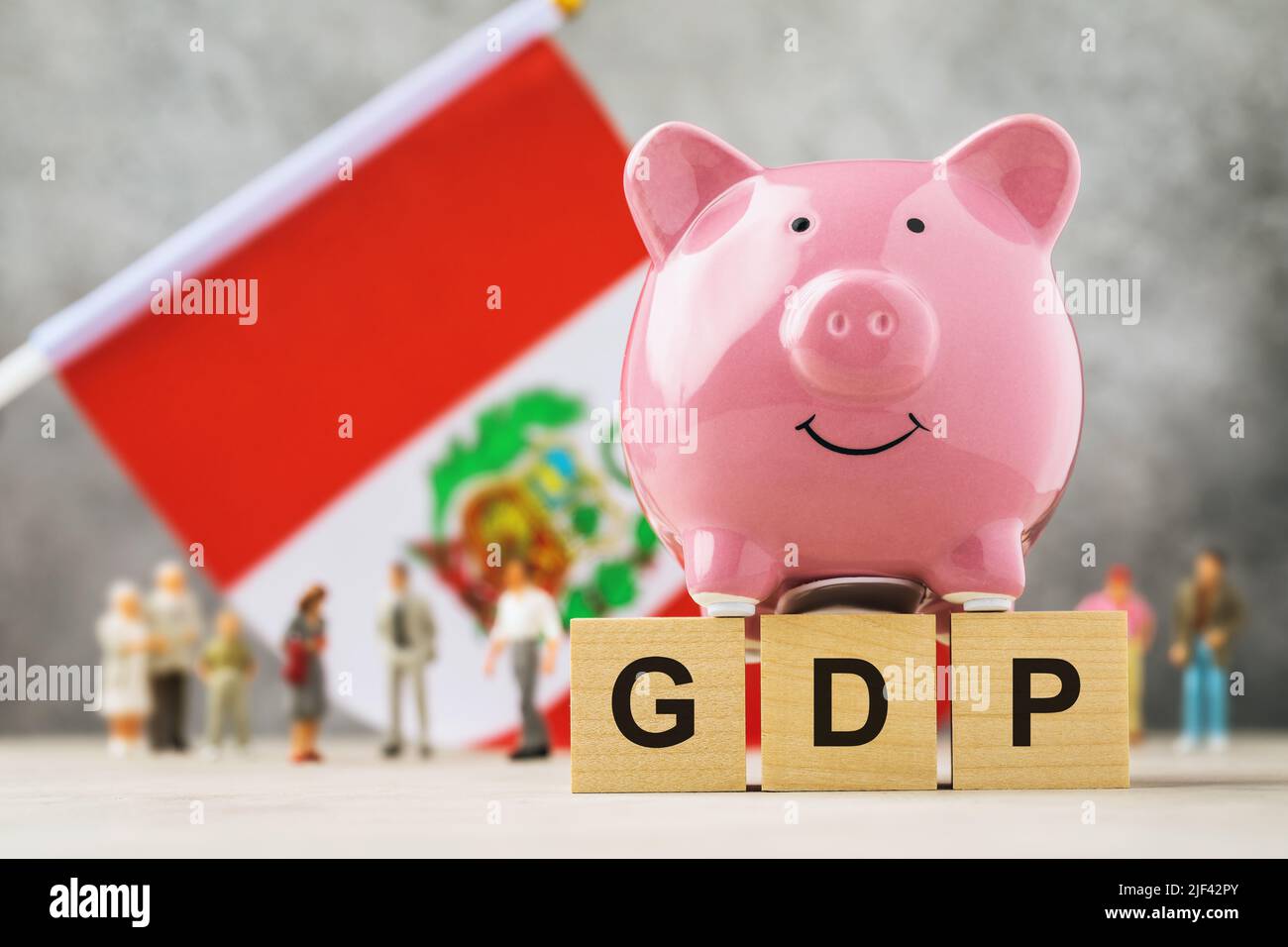 Banco de cerdos, cubos de madera con texto, gente de juguete de plástico y una bandera sobre un fondo abstracto, un concepto sobre el tema del PIB del Perú Foto de stock