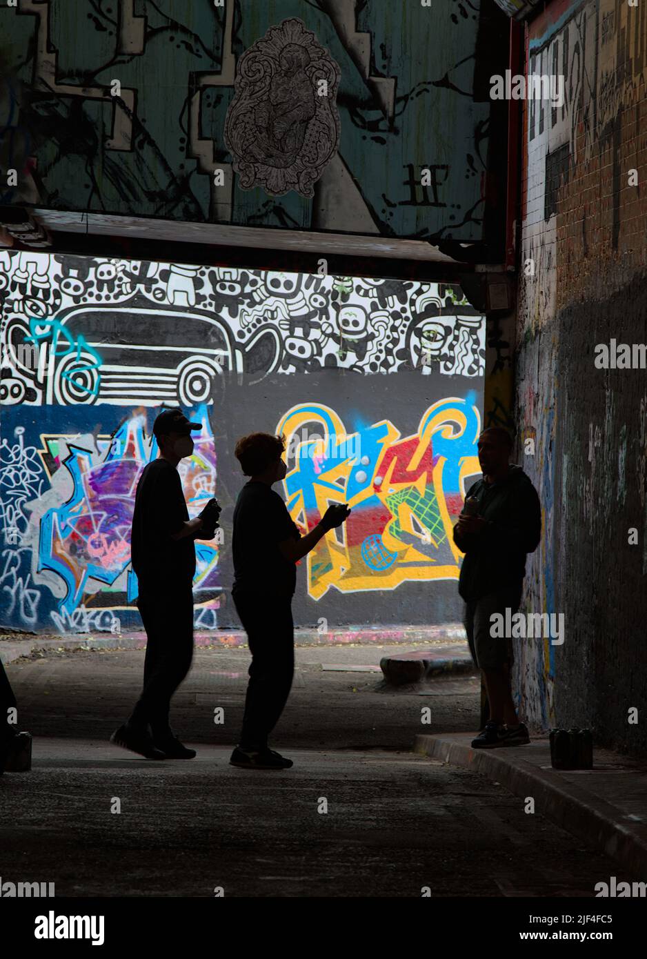 Silueta de los artistas de Graffiti con latas de spray bajo un puente en Un túnel cerca de la estación de Waterloo, Londres, Reino Unido Foto de stock