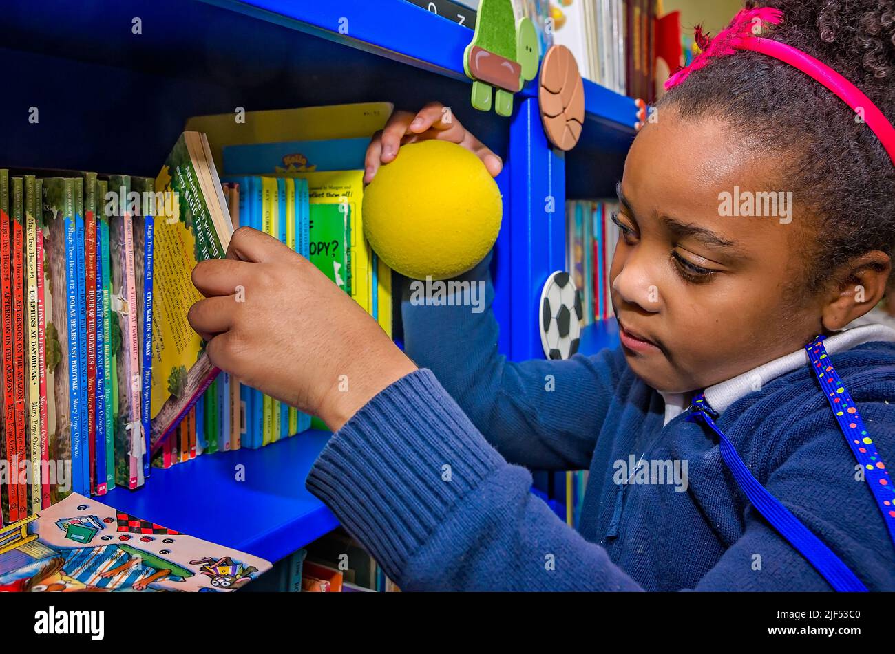 Una niña afroamericana elige un libro de una estantería durante un programa extraescolar, el 28 de febrero de 2013, en Columbus, Mississippi. Foto de stock