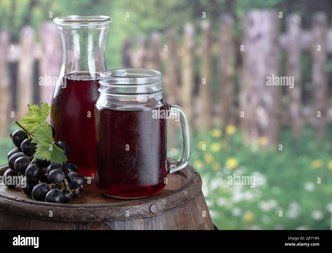 Vaso de jugo de uva y uvas frescas sobre un cañón rústico de madera con fondo rural Foto de stock
