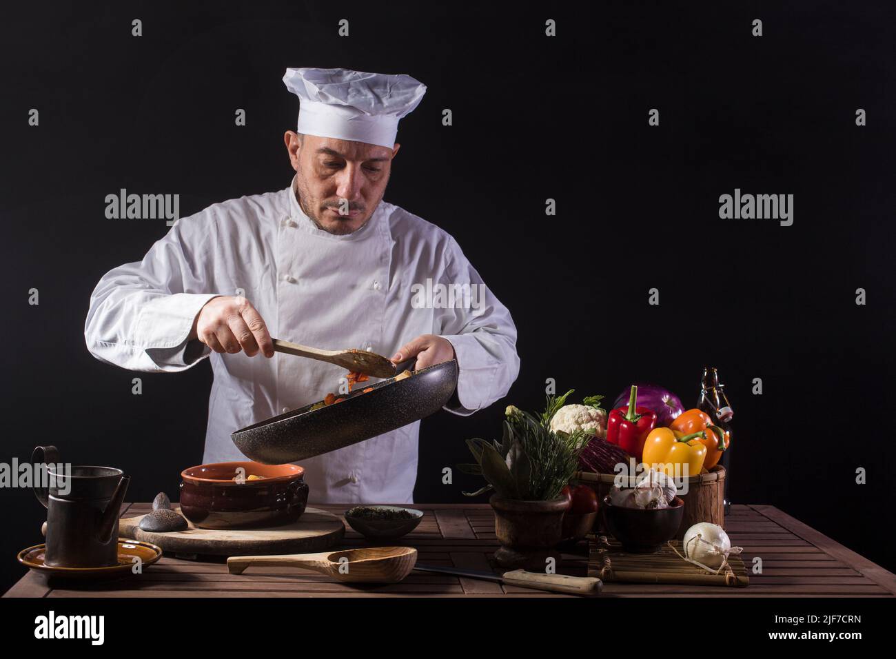 Chef masculino con uniforme blanco preparando plato de comida con verduras antes de servir mientras trabaja en una cocina de restaurante Foto de stock