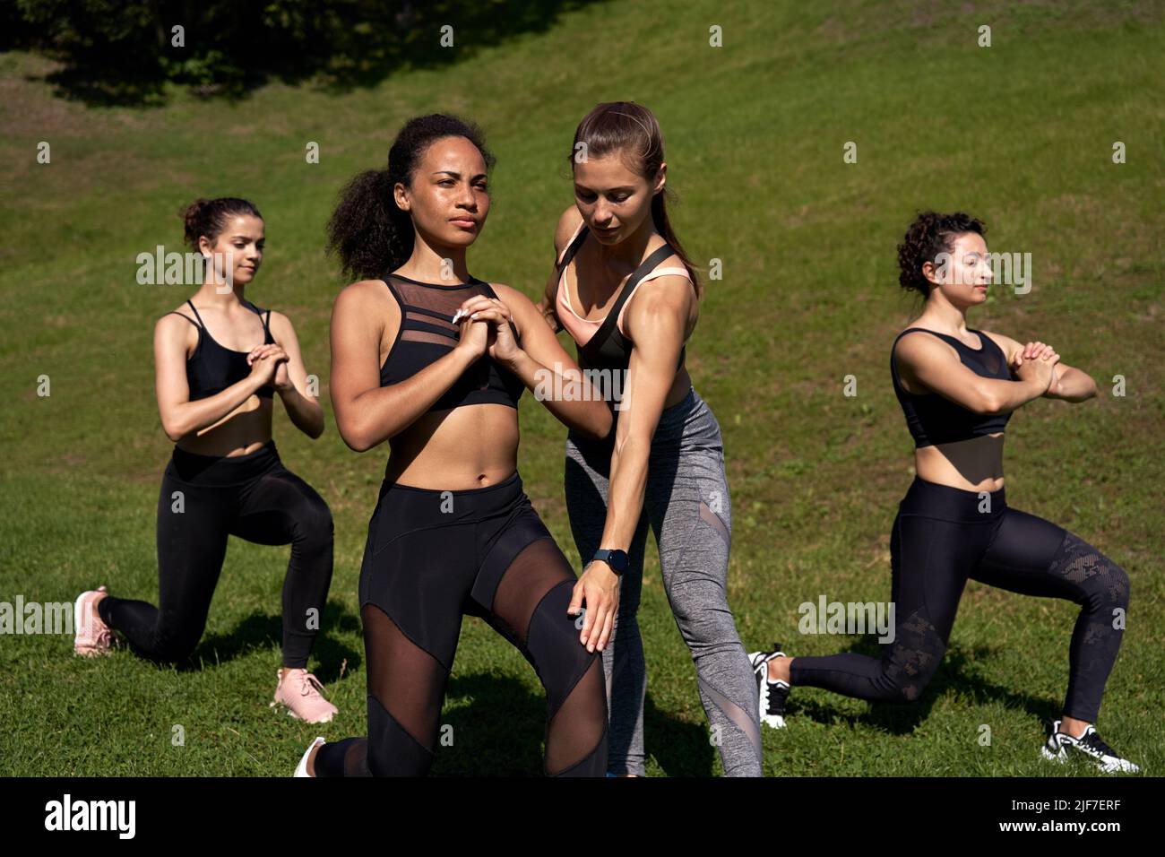 Entrenador deportivo en forma que ayuda a una mujer africana a aprender lunge en clase al aire libre en grupo. Foto de stock