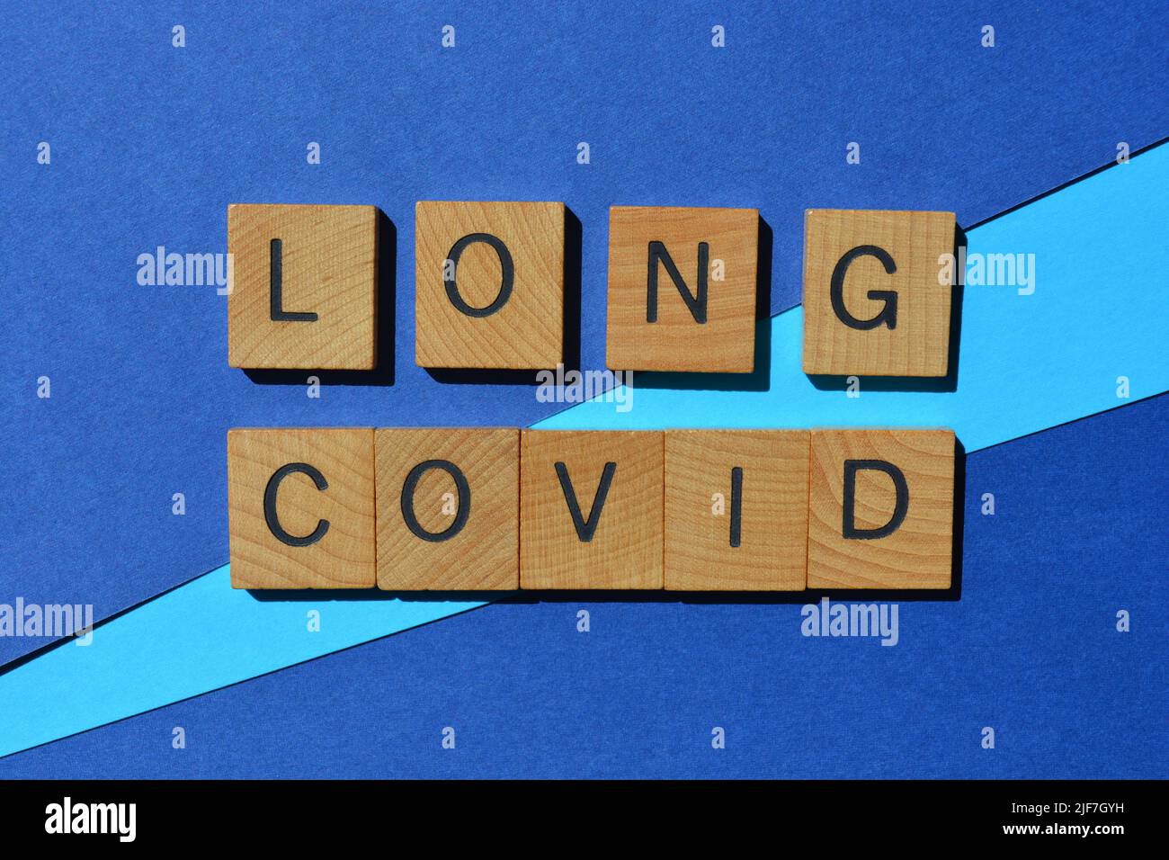 Covid largo, palabras en letras de madera del alfabeto aisladas sobre fondo azul Foto de stock