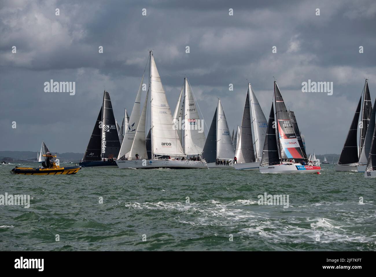 Los competidores se alinean y pasan por el barco de patrulla del puerto amarillo para iniciar la carrera anual del club de vela de la isla de Wight Round the Island Foto de stock