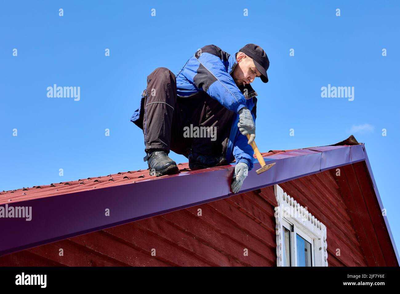 El carpintero está reparando el hierro del techo de la casa en el país. Foto de stock