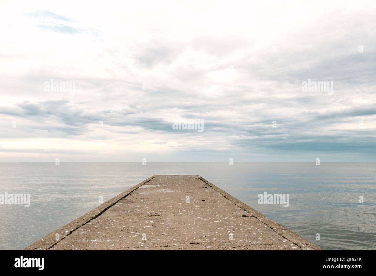 Muelle de hormigón vacío al mar con cielo dramático y aguas tranquilas, malecón industrial abandonado Foto de stock