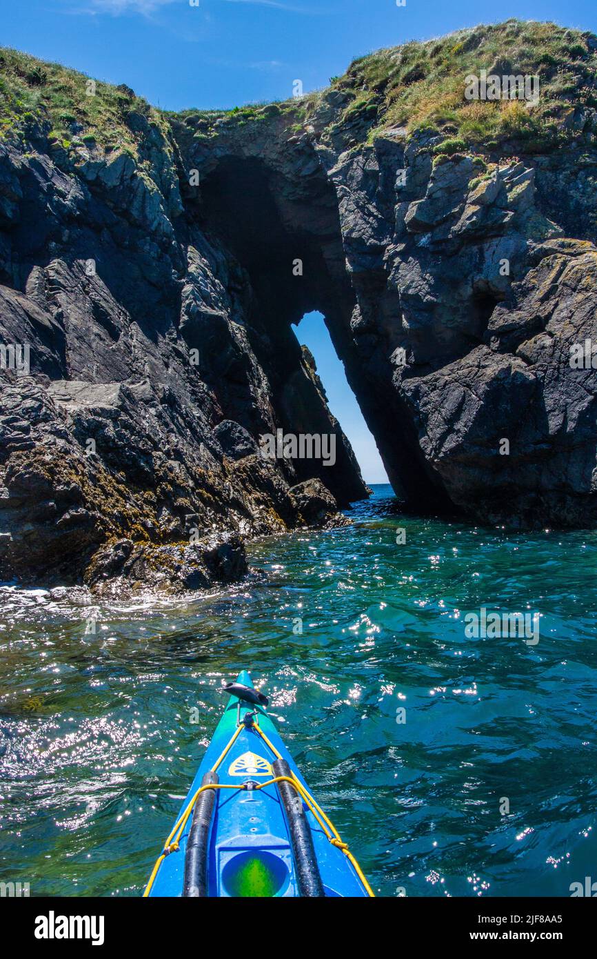 Kayak de mar a través de un arco rocoso en la costa de Pembrokeshire, en Gales Foto de stock