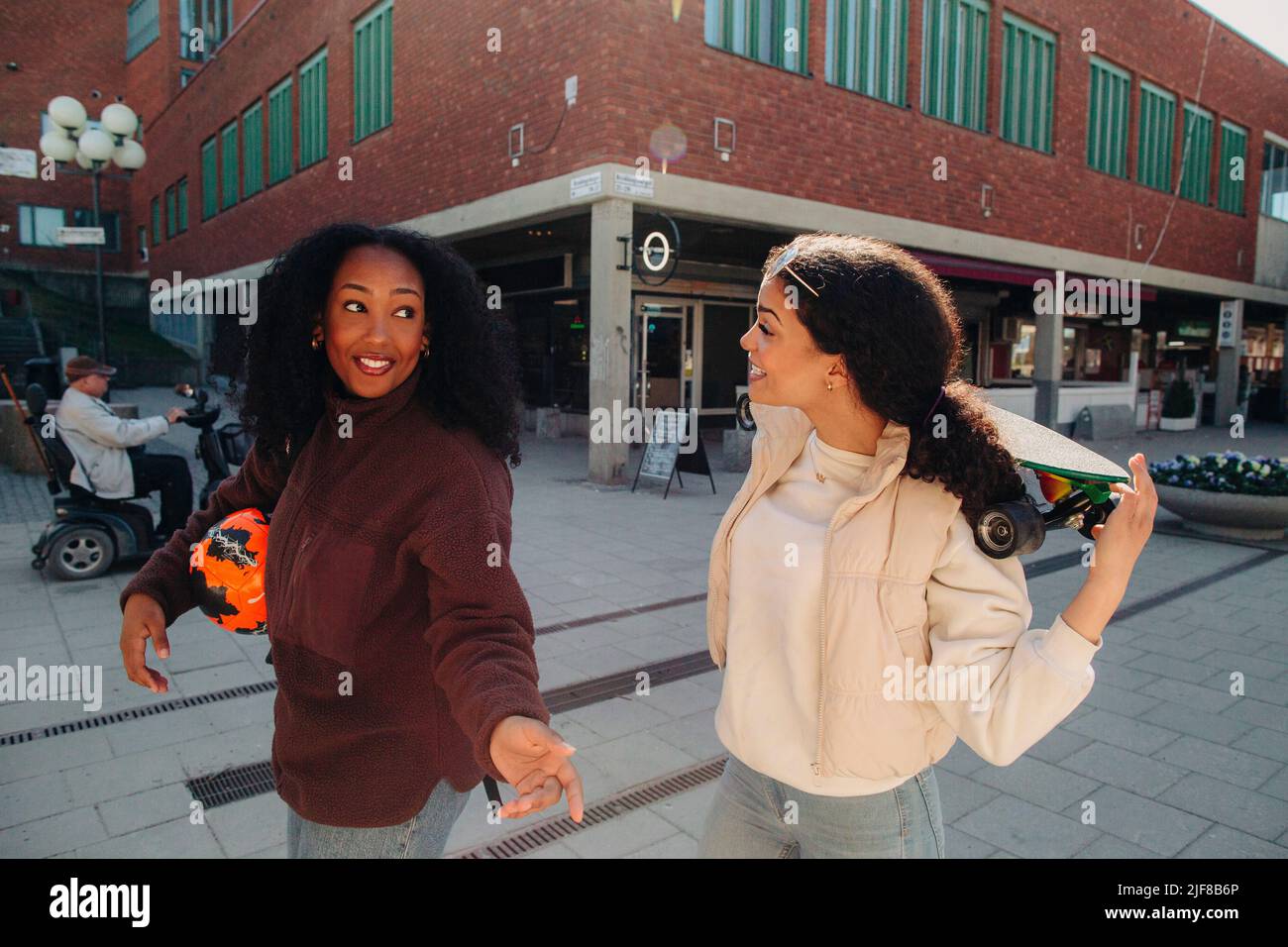 Mujer joven hablando con una amiga mientras camina por la calle Foto de stock