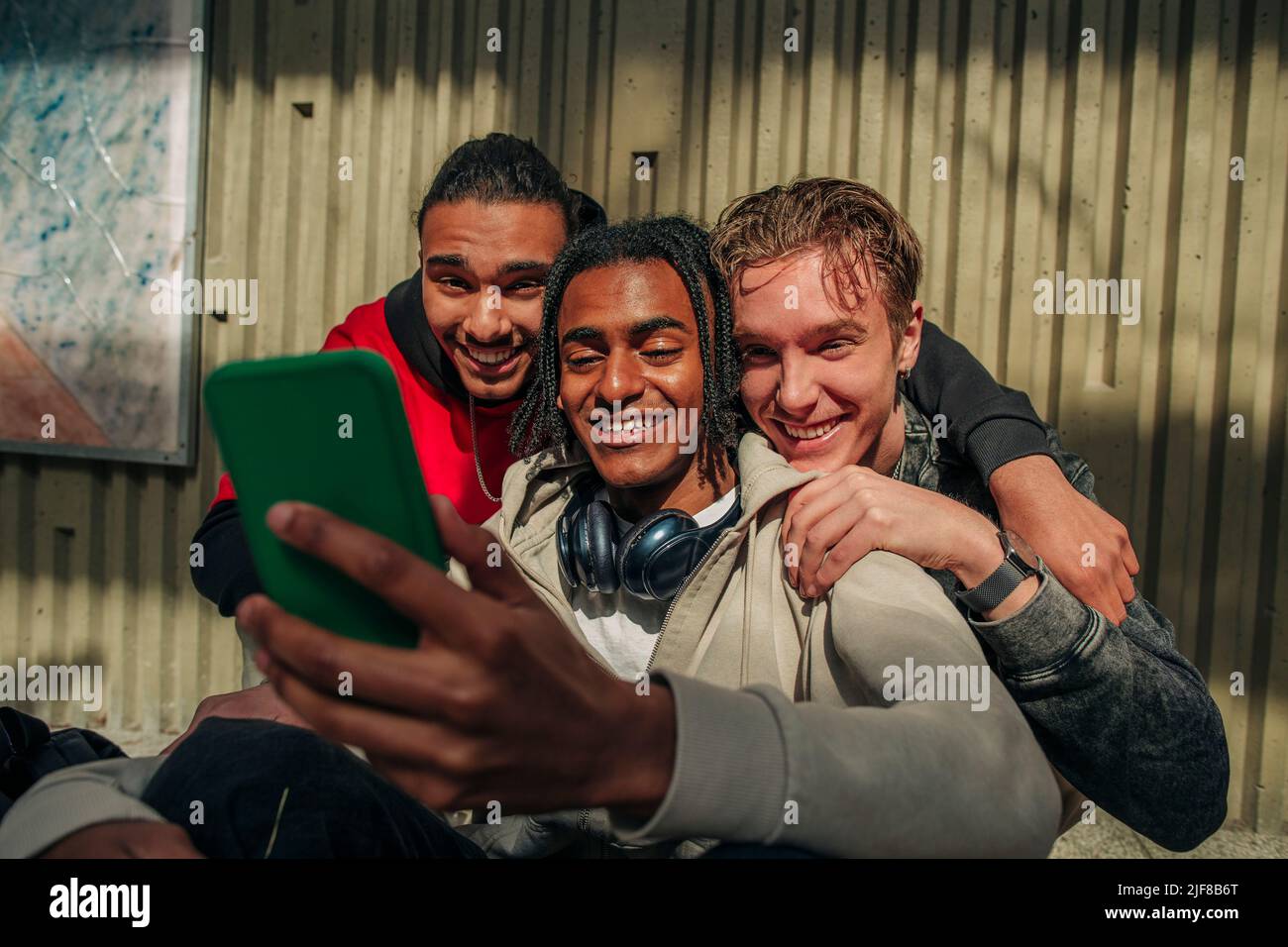 Sonriendo amigos hombres multirraciales haciendo videollamadas a través del teléfono inteligente contra la pared Foto de stock
