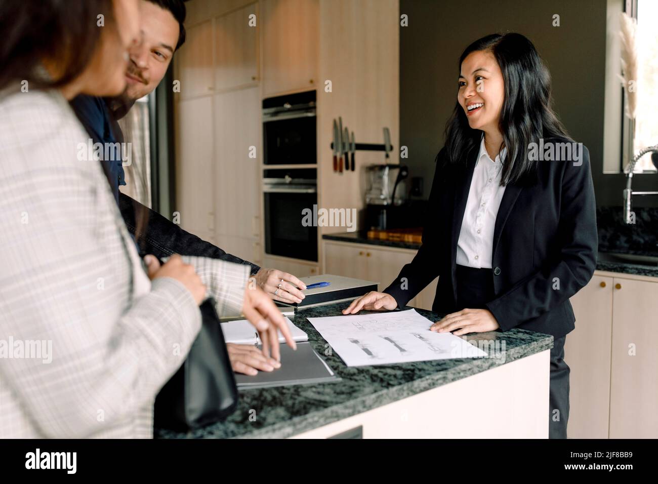 agente inmobiliario sonriente que explica los documentos de la nueva casa a los clientes Foto de stock