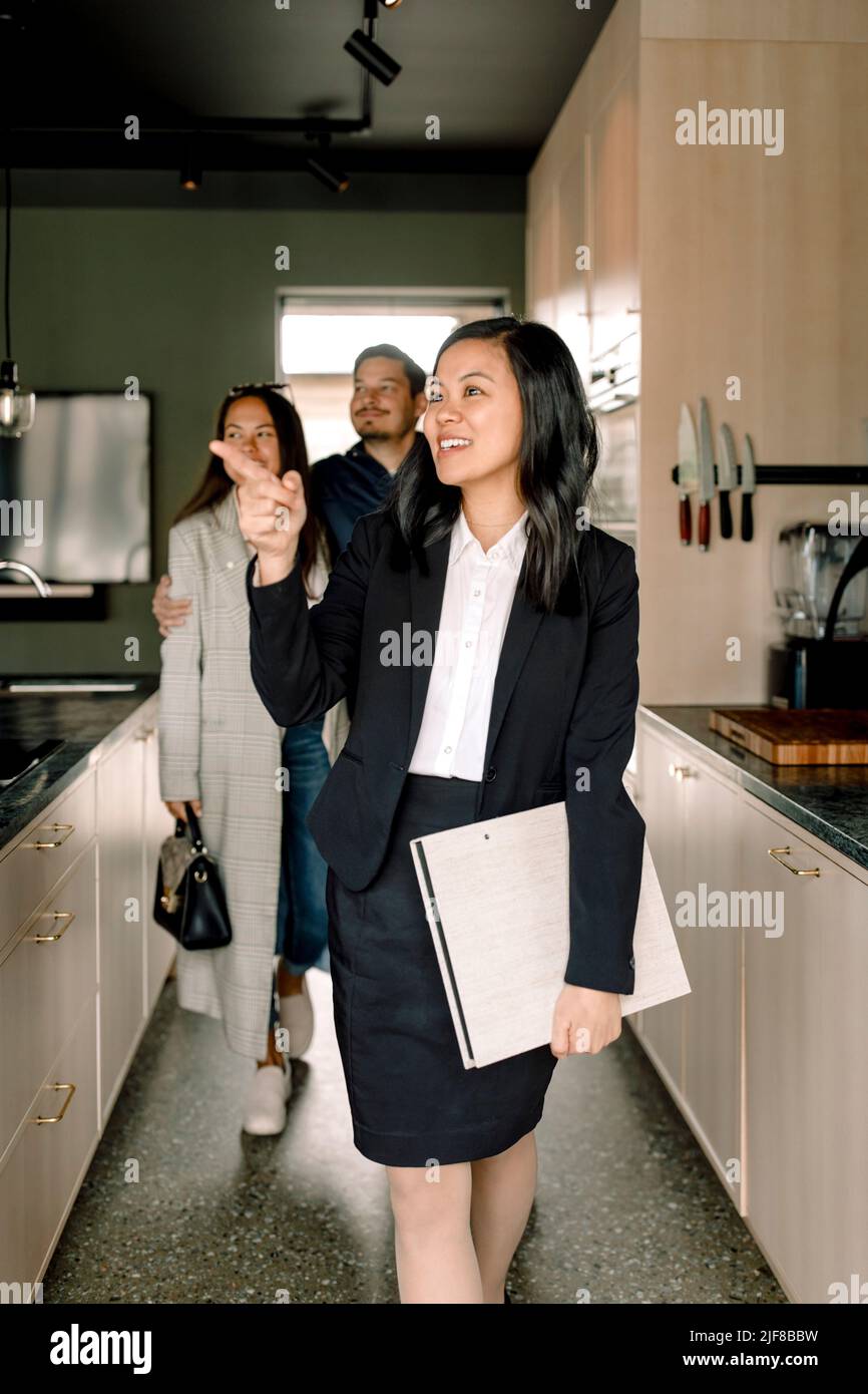Inmobiliaria señalando mientras que muestra el área de la cocina a los clientes en la casa nueva Foto de stock