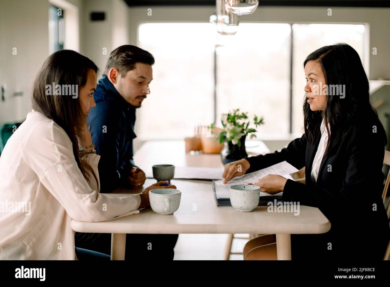 Clientes discutiendo documentos de propiedad con una vendedora en la mesa de la casa nueva Foto de stock
