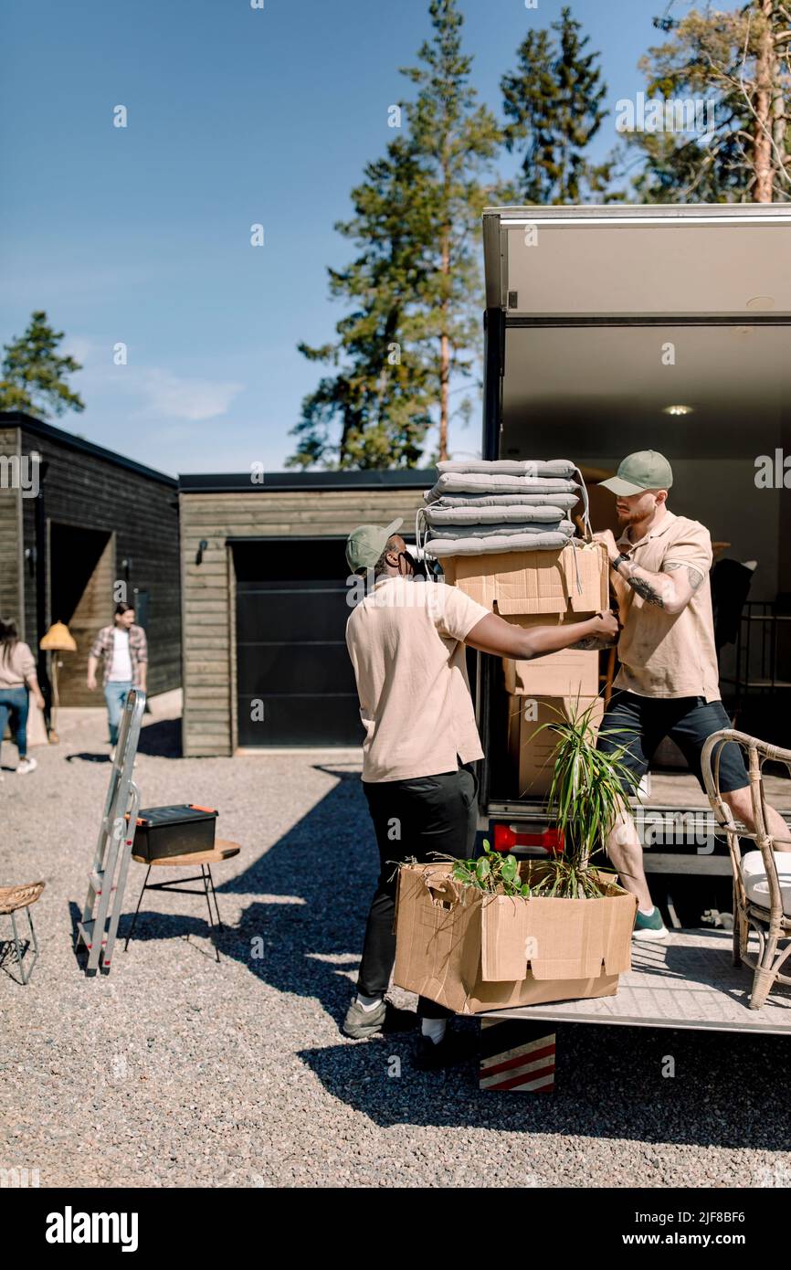 Los hombres de la entrega recogen cajas de cartón del camión durante el día soleado Foto de stock
