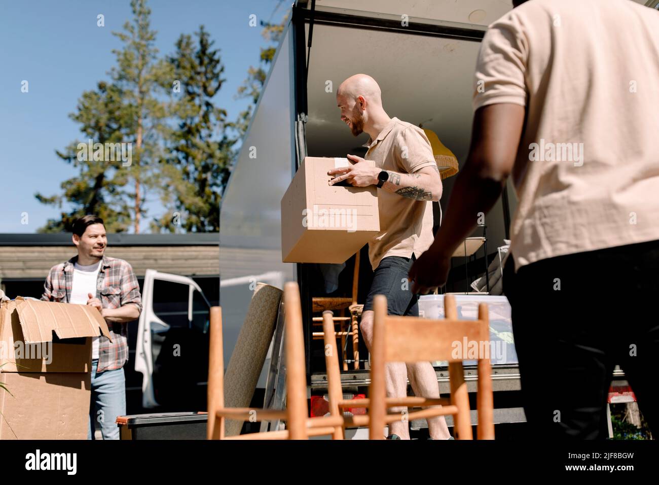 Empleados de la empresa de entrega que ayudan al hombre a descargar cajas del camión Foto de stock