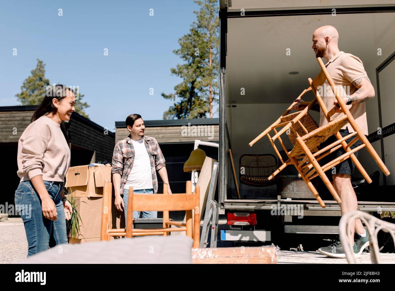 Pareja mirando al transportador descargando sillas del camión en un día soleado Foto de stock