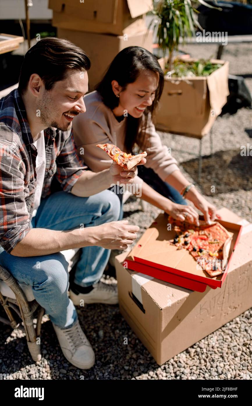 Pareja sonriente comiendo pizza mientras se mudan en casa nueva Foto de stock
