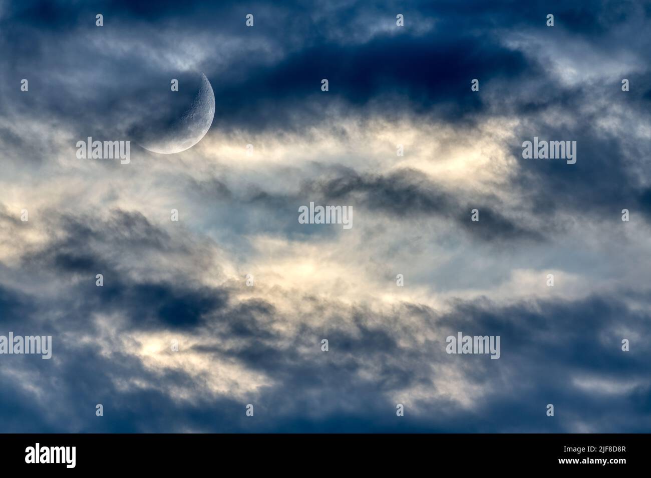 La Luna se eleva entre Un colorido cielo de puesta de sol lleno de nubes Foto de stock