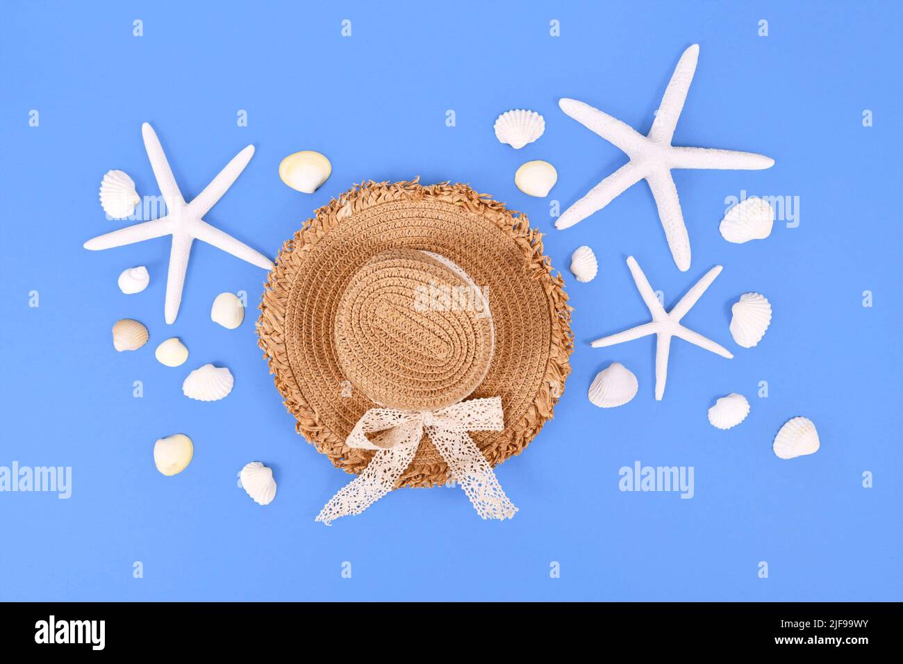 Estrella de mar blanca, conchas marinas y sombrero de paja de verano sobre fondo azul Foto de stock