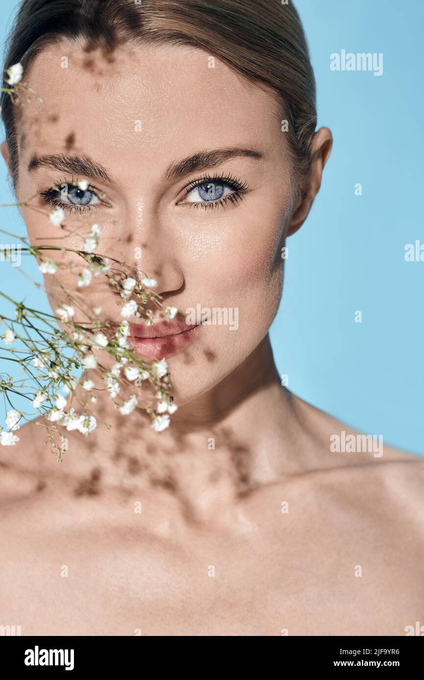Retrato de belleza de una joven caucásica con sana piel facial hidratada y ojos azules con flores. Concepto de cuidado de la piel Foto de stock