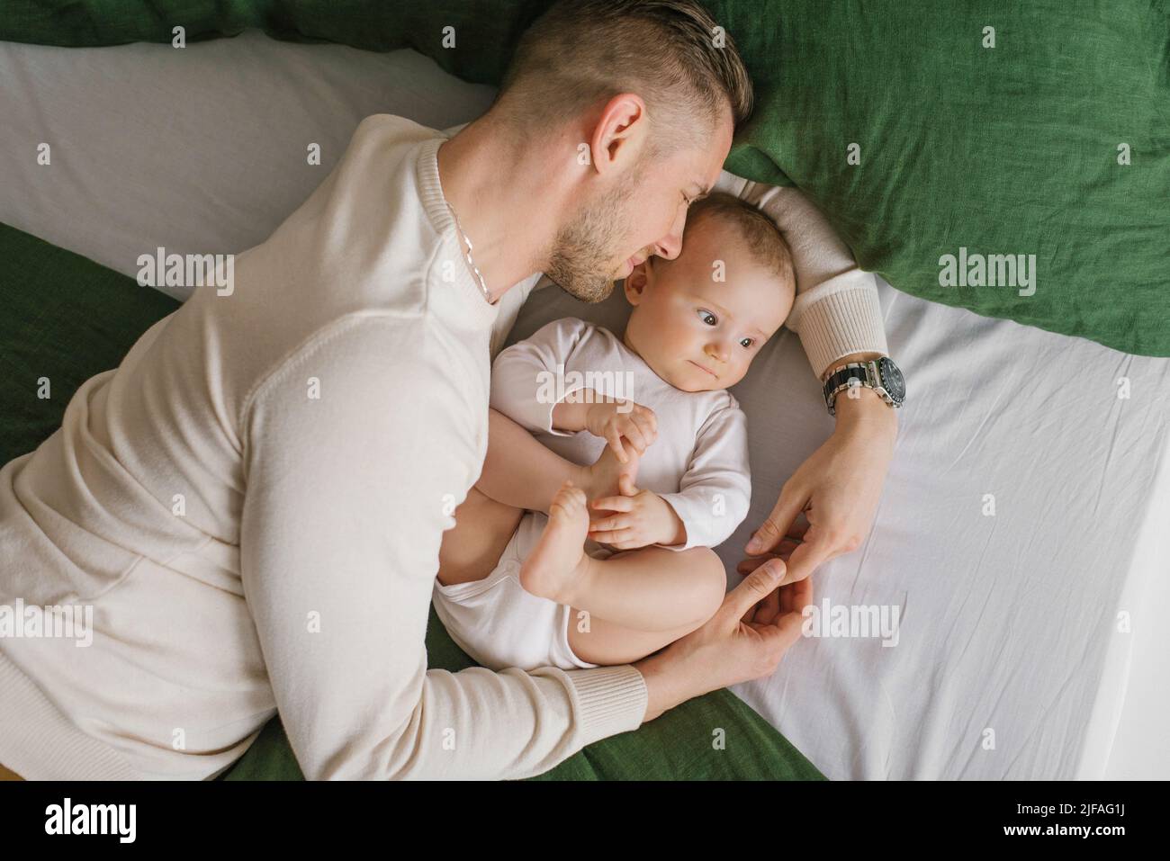 Un padre amoroso yace en la cama con su bebé y lo abraza Foto de stock