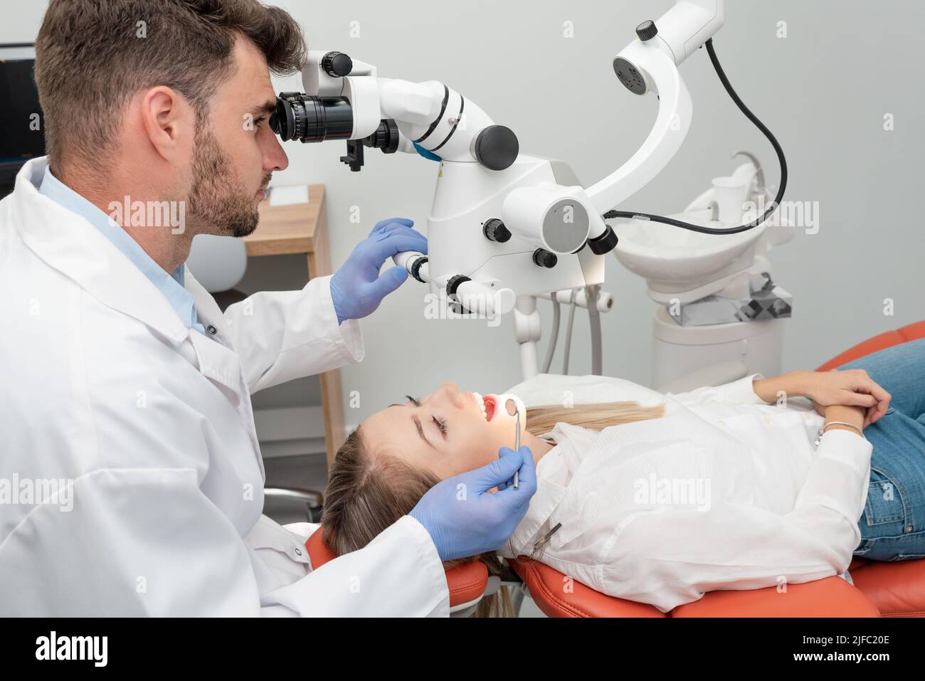 Dentista masculino trabajando con microscopio dental. Abra la boca de la mujer durante el examen oral en el dentista Foto de stock