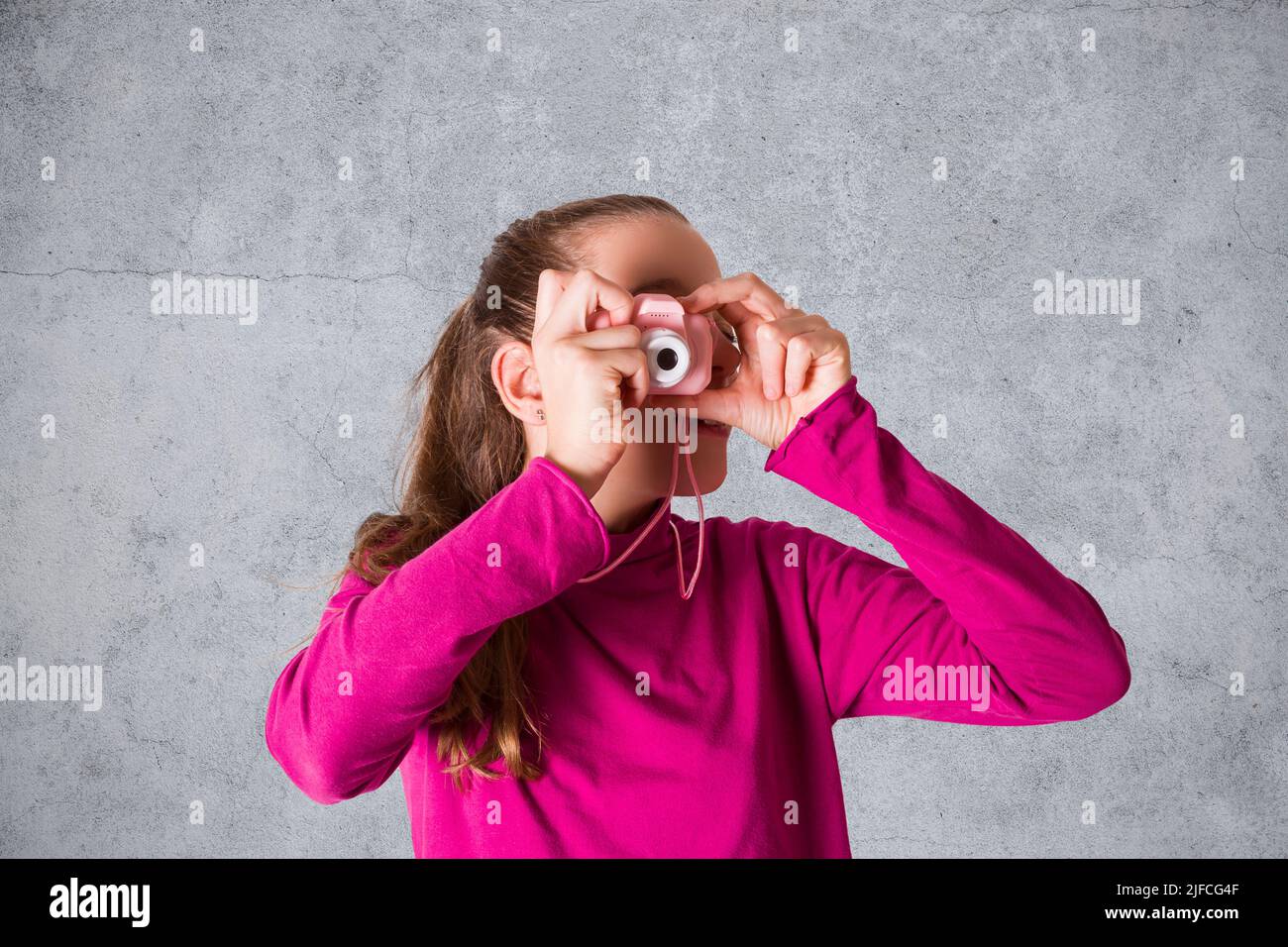 Little Girl está tomando una fotografía con la cámara de fotos de juguete sobre fondo gris Foto de stock