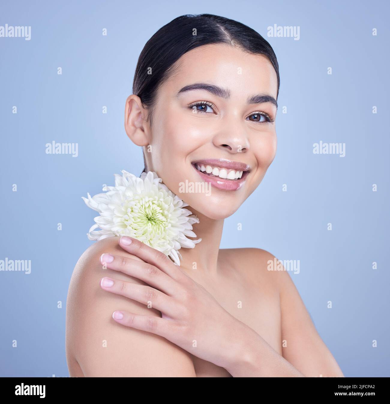 Retrato de estudio de una hermosa mujer de raza mixta posando con una flor. Jóvenes hispanos usando un tratamiento orgánico para el cuidado de la piel contra un copyspace azul Foto de stock