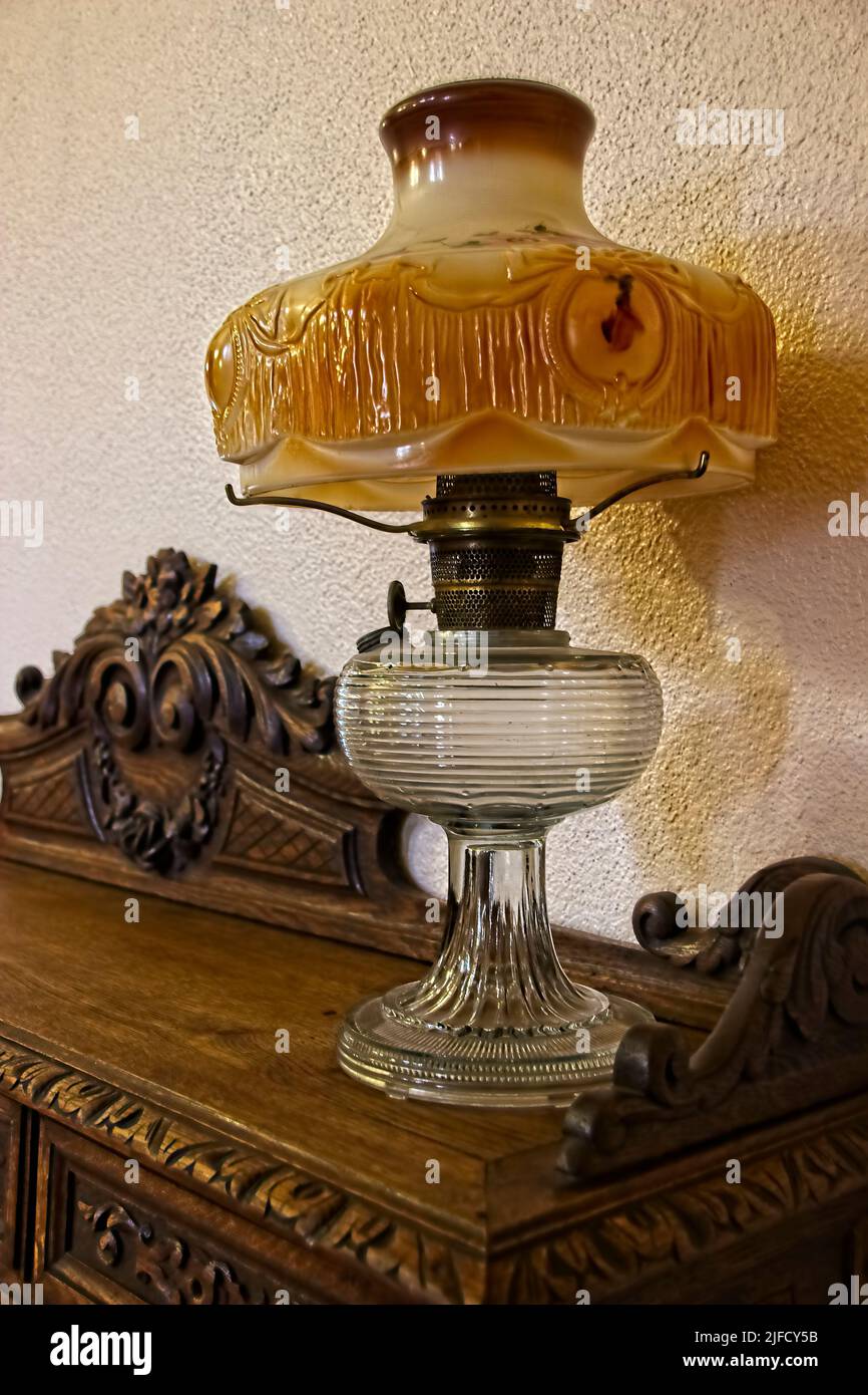 Esta fotografía cuenta con una hermosa lámpara de aceite de ámbar de finales del siglo pasado, colocada sobre una mesa lateral de madera finamente tallada. Foto de stock