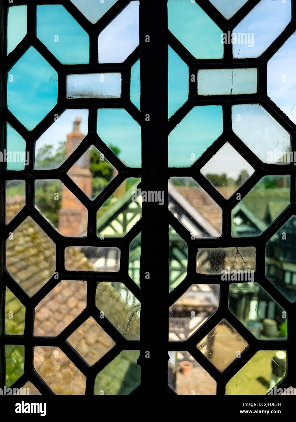 La vista borrosa a través de una ventana de vidrio del siglo 16th en Little Moreton Hall, una casa señorial Tudor con entramado de madera cerca de Congleton en Cheshire, noroeste E Foto de stock