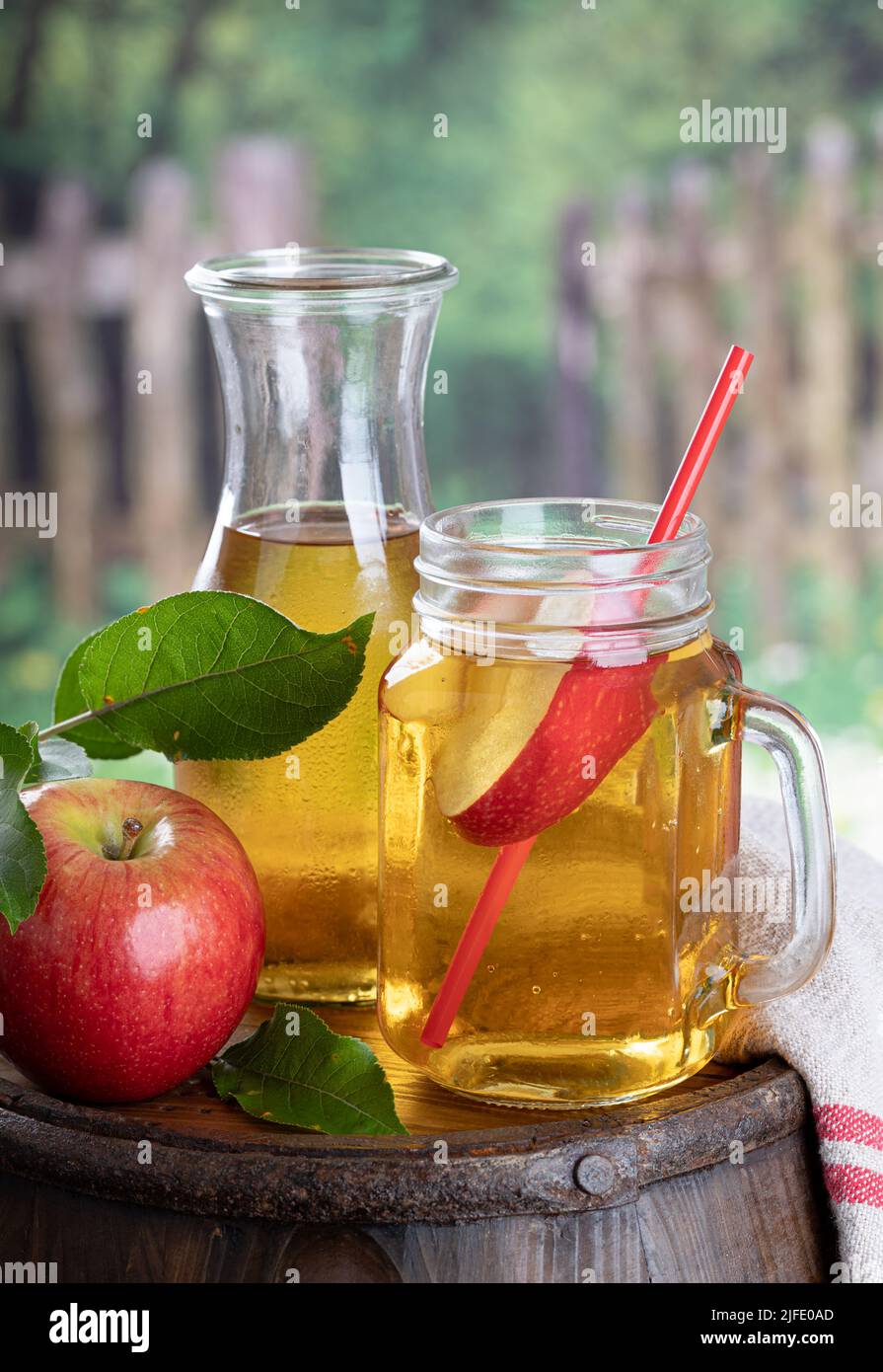 Vaso de zumo de manzana con rodaja de manzana sobre un viejo barril de madera con fondo rural Foto de stock