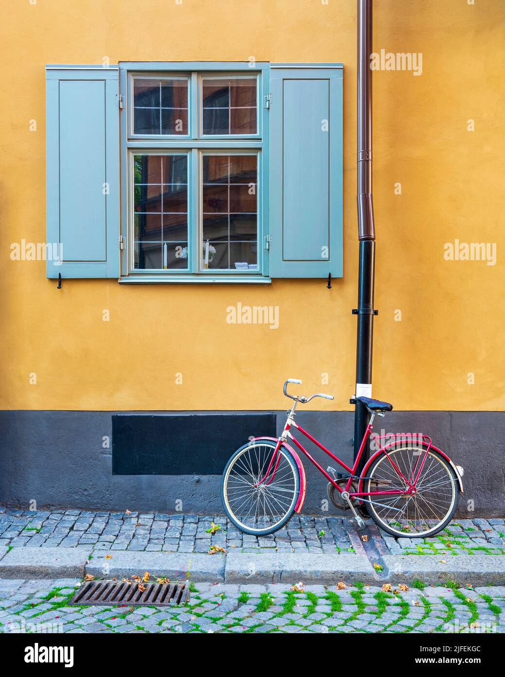 Bicicleta roja aparcada bajo una ventana antigua y tradicional con persianas azules en una pared naranja en una calle estrecha de adoquines en el casco antiguo de Gamla Stan, Estocolmo, Suecia Foto de stock