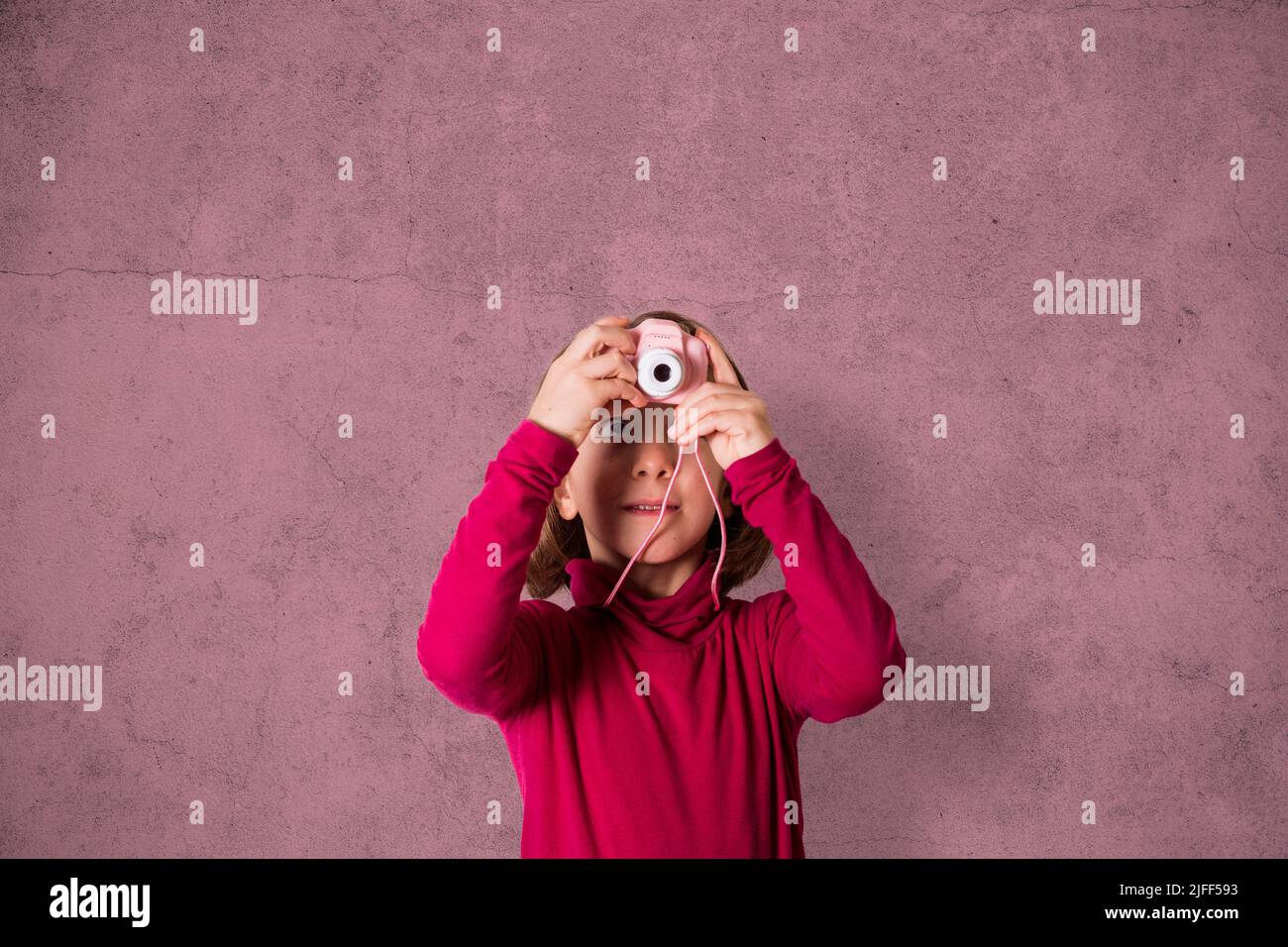 Little Girl está tomando una fotografía con la cámara de fotos de juguete sobre fondo rosa Foto de stock
