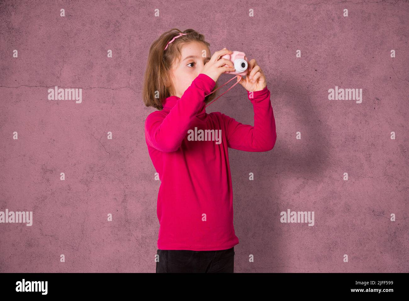 Little Girl está tomando una fotografía con la cámara de fotos de juguete sobre fondo rosa Foto de stock