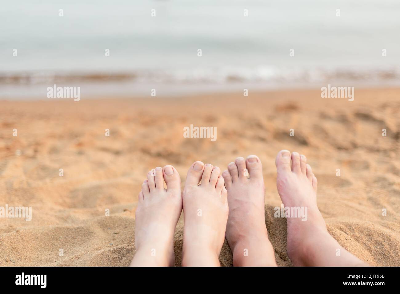 Primer plano de los pies de mujer y hombre relajándose en la playa de arena con el lago en el fondo Foto de stock