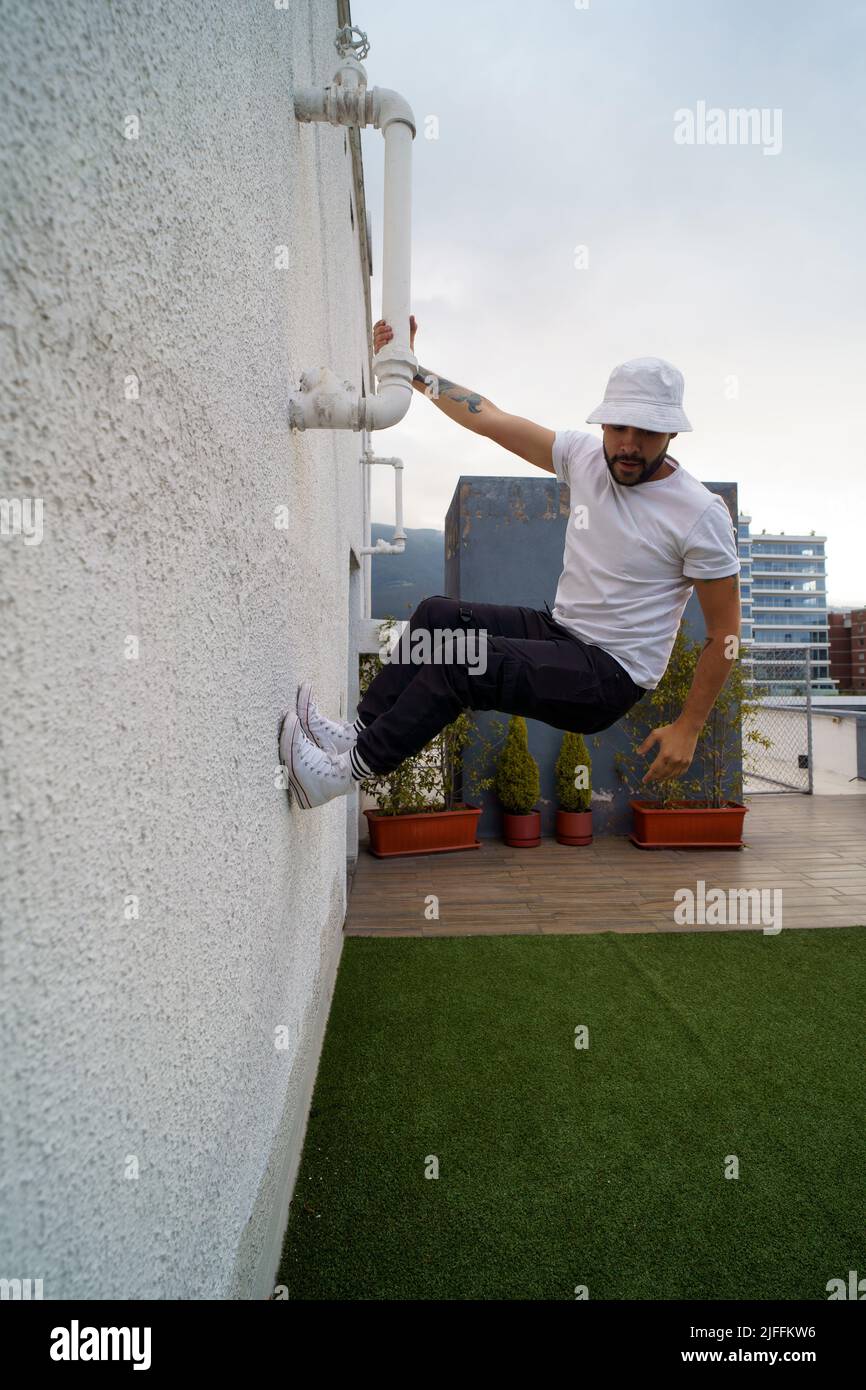 el hombre joven lleva camiseta blanca, jeans y gorra saltando a la pared, estilo de vida urbano, practicando parkour para el entrenamiento diurno Foto de stock